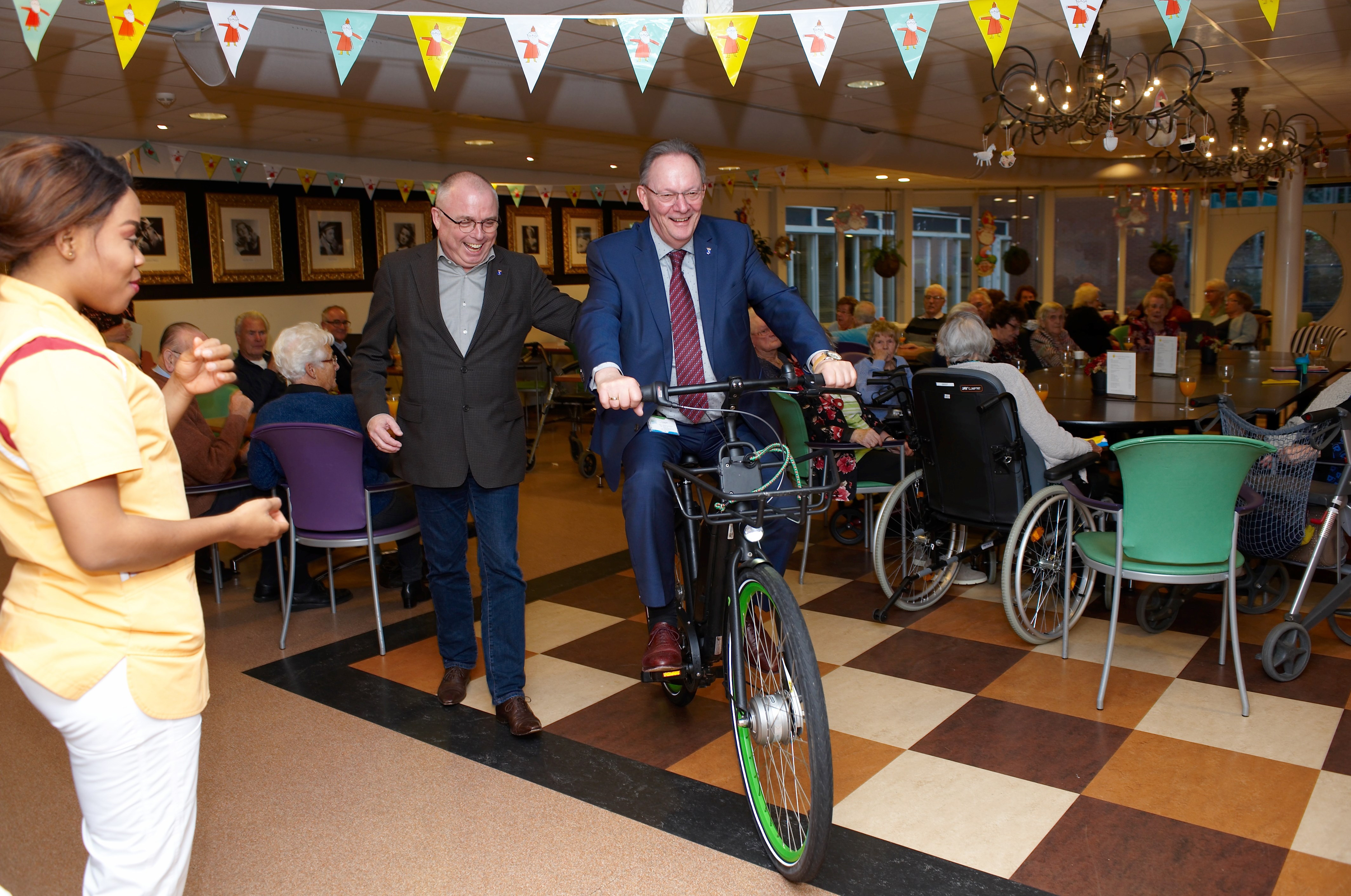 Burgemeester Peter Tange en wethouder Jeroen Schalkwijk van Wormerland fietsen een rondje door de zaal van Zorgcirkel Torenerf ter gelegenheid van het Bronzen Milieukenmerk dat Torenerf ontving. 